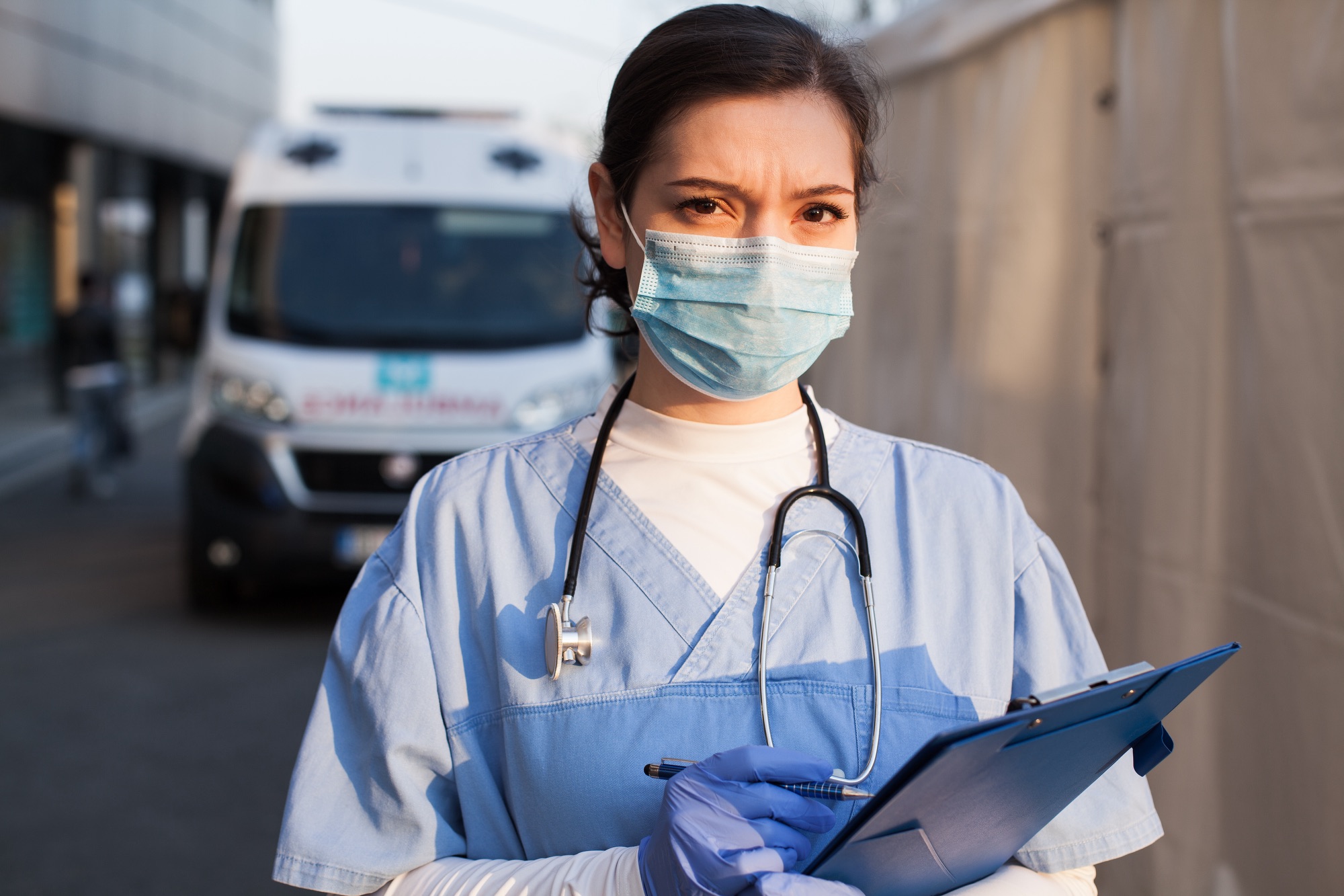 SS_Young female NHS UK EMS doctor in front of healthcare ICU facility,wearing protective face mask holding medical patient health check form,Coronavirus COVID-19 pandemic outbreak crisis PPE shortag